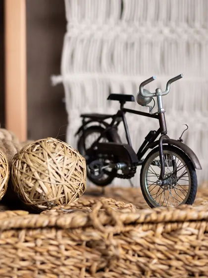 A close-up of decor details from a boho baby shower. A miniature bicycle and woven twine balls are placed on rustic wicker baskets, adding to the natural and handcrafted feel.