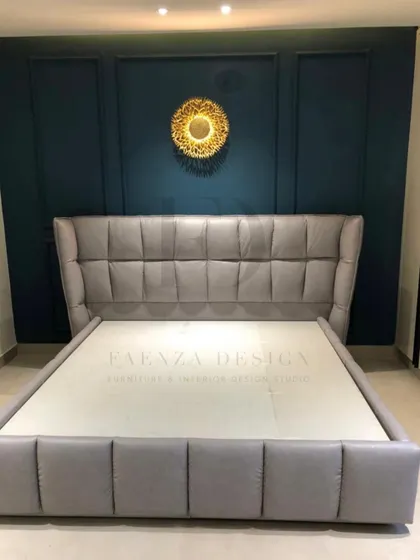 This grey tufted bed with a winged headboard is set against a deep teal paneled wall, creating a bold and dramatic contrast. The gold sunburst mirror adds a final decorative touch.