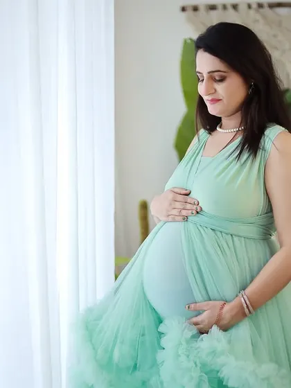 A profile view showcasing a beautiful mint green gown. The soft light from the window highlights the baby bump and the delicate fabric of the dress.