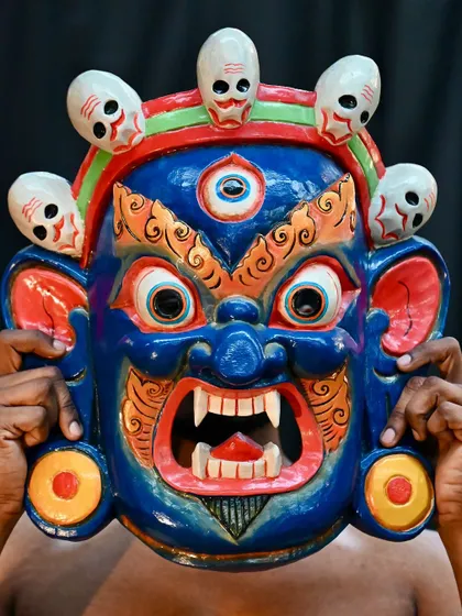 A close-up of a vibrant blue Nepali mask, showcasing the detailed painting and the skulls that adorn it. These masks depict various deities and are believed to protect against bad luck.