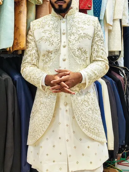A client wearing a hand-embroidered open sherwani in a beautiful off-white color. The layered look with a shorter embroidered jacket over a longer kurta is a modern favorite.