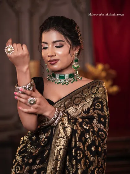 A full shot of the model adjusting her jewelry, showing the complete styling for the elegant black saree look.