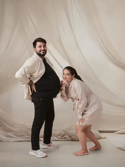 A fun and playful moment from a modern studio shoot. The mom-to-be playfully checks on her partner's "bump," adding a touch of humor to the session.