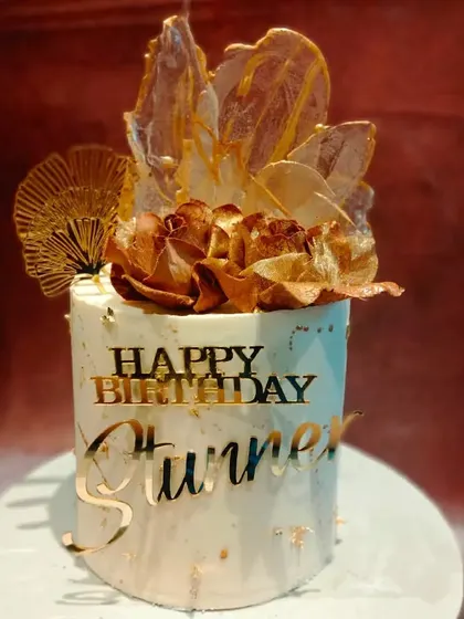 A stunning cake for a "stunner." This design features golden roses and abstract sail toppers, creating a piece of edible art that is both modern and glamorous.