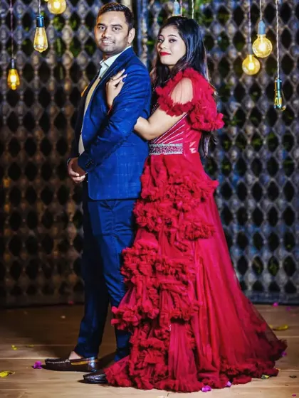 A classic pre-wedding pose. The couple looks elegant and happy, with her in a beautiful red ruffle gown and him in a sharp blue suit.