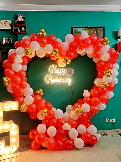 A vibrant 5th-anniversary heart-shaped balloon arch in red and white, with a light-up number '5' and a neon sign.