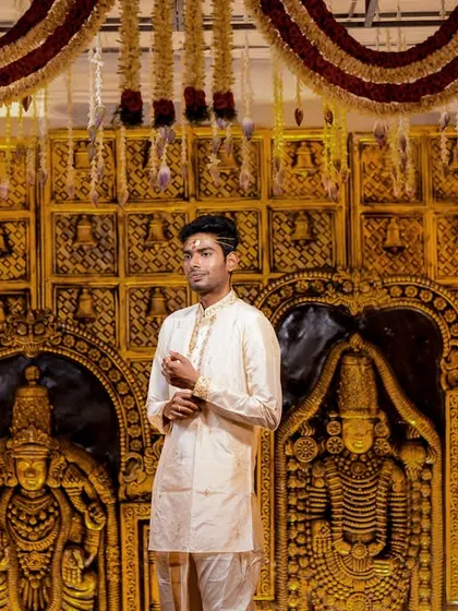 A groom stands before a magnificent, traditional golden temple-style backdrop at his Pondicherry wedding.