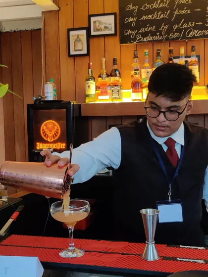 A bartender in classic uniform, focused on his craft as he pours a freshly shaken cocktail. We pride ourselves on the precision and care we put into every single drink.
