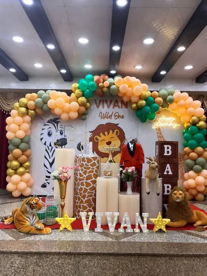 Welcome to the jungle! This "Wild One" themed birthday party is full of fun details. The setup includes a custom backdrop with cartoon lions and zebras, a lush balloon arch in safari colors, and plush animal props like a tiger and lion to bring the theme to life for the little one.