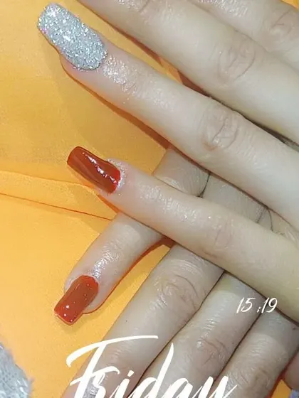 A chic and simple design featuring a rich, burnt-orange polish on square nails, paired with a single, statement-making silver glitter accent nail.