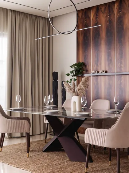 The dining area is defined by a stunning mahogany wood accent wall. The warm tones of the wood are complemented by the soft beige dining chairs and a modern, linear chandelier, creating an elegant space for entertaining.