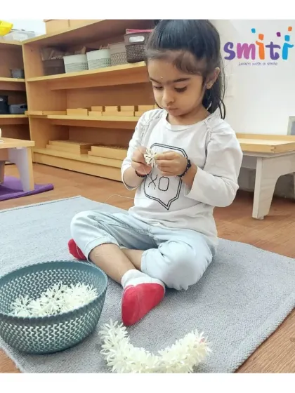 A little girl practices the delicate task of stringing jasmine flowers. This practical life activity enhances her fine motor skills and concentration while connecting her with a beautiful cultural tradition.