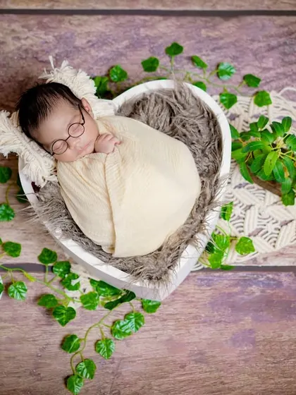 A wise little soul. This overhead shot shows a baby nestled in a heart-shaped bowl, surrounded by greenery for a natural, earthy look.