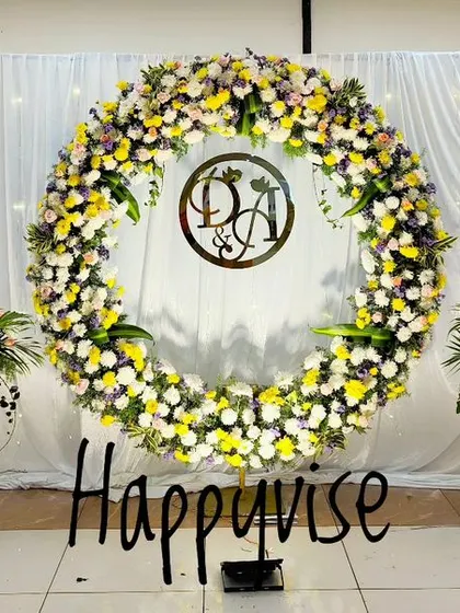 This full-stage setup features a large floral wreath with a custom monogram at its center. The design is balanced with floral arrangements on pedestals, creating a grand and personalized look for a reception.