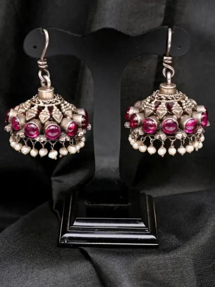 A studio shot of the silver and red stone jhumkha earrings on a display stand, emphasizing their form and the drops of pearls.