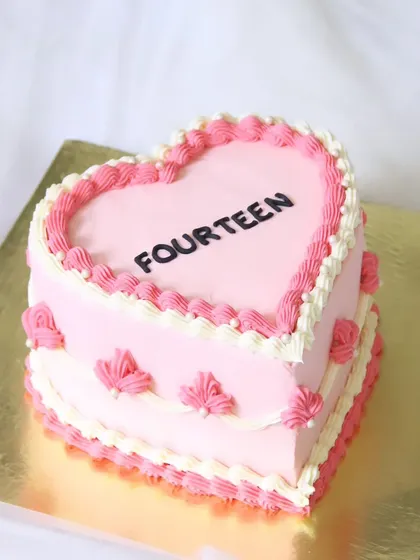 A charming vintage-style heart-shaped cake for a 14th birthday. The cake is decorated with classic pink and white shell piping for a sweet and nostalgic feel.