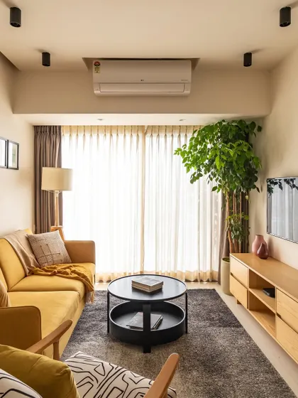The living room, with its vibrant mustard sofa, abstract rug, and large planter. The space is a perfect blend of modern design and natural elements.