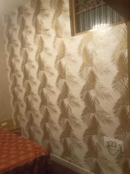 A bedroom wall with a textured wallpaper featuring a golden feather pattern. The metallic sheen adds a touch of glamour and luxury.
