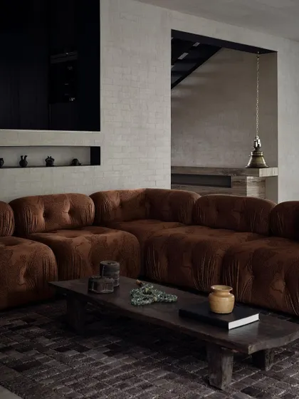 The living room, with its rich brown velvet sofa and dark wooden coffee table, is a cozy and inviting space. The traditional brass bell in the background adds a unique, cultural element.