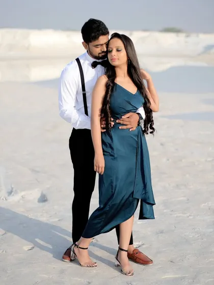 A couple poses in a stark, white sand landscape, creating a minimalist and elegant pre-wedding portrait. The groom's suspenders and the bride's teal dress add a pop of classic style.