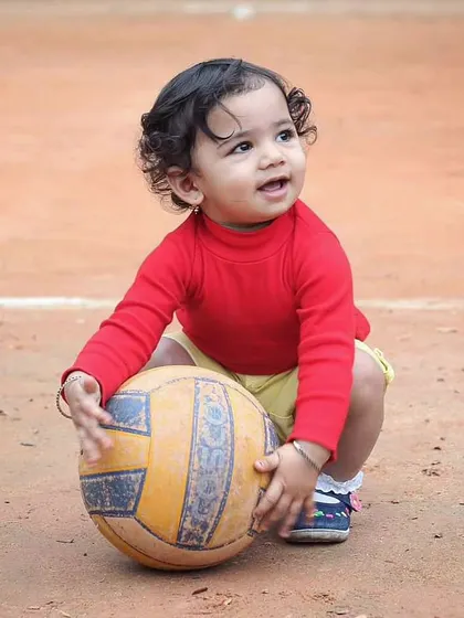 All work and no play makes for a dull day. This outdoor shot captures a toddler's curiosity and engagement while playing with a ball.