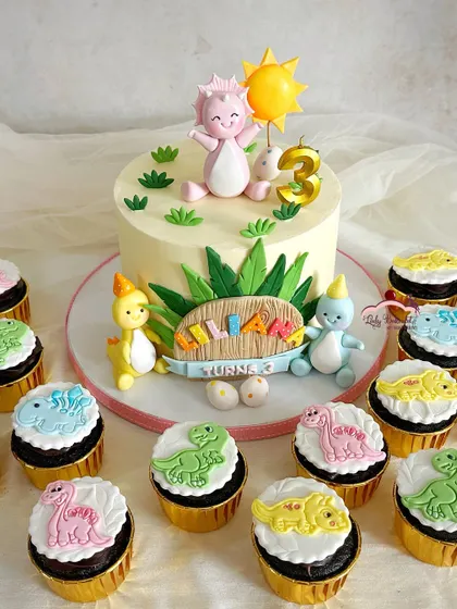 A truly 'Dino-mite' celebration for a third birthday. The friendly pink dinosaur on top of the cake is the main character, surrounded by a whole party of colorful dino friends on the matching cupcakes.