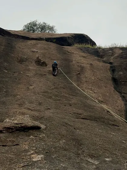 A wide view showing a climber ascending a large rock face, highlighting the scale of the challenge.