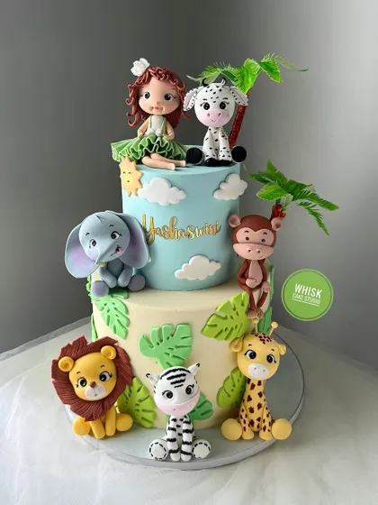 A jungle-themed cake designed for a girl. This two-tiered cake features a girl figurine with her animal friends, including a dalmatian, monkey, and lion.