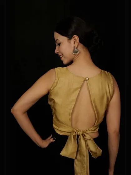 This sleeveless golden blouse has a keyhole back with a chic bow tie-up at the bottom, creating a modern and playful look.