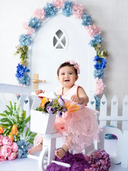 A bright and happy first birthday photoshoot with a floral theme. This little girl's smile lights up the whole studio as she sits on her flower-filled tricycle.