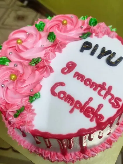 Celebrating a sweet milestone with this "9 months complete" cake. It features a half-and-half design with pink piped rosettes and a personal message.