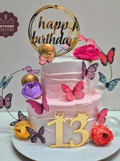 A lovely two-tier butterfly-themed cake for a 13th birthday. The pink ombre frosting is decorated with a cascade of butterflies and fresh flowers, marking the transition into the teenage years.