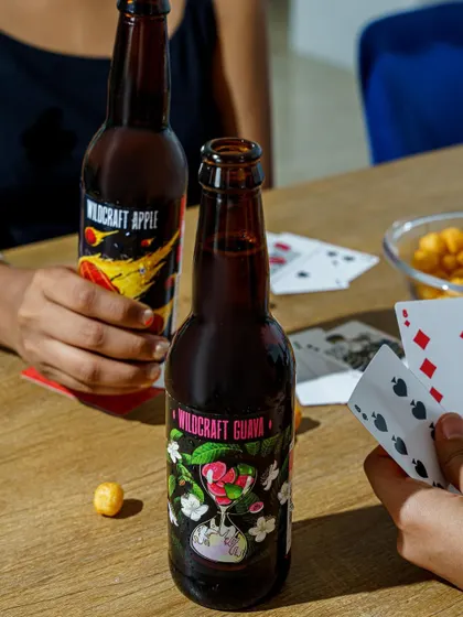 Lifestyle product photography for Wildcraft beverages. This shot places the product in a social setting, suggesting a fun, relaxed moment with friends.