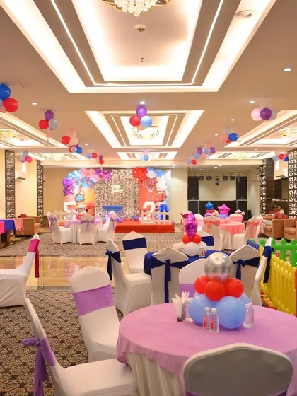 A full view of a banquet hall prepared for a birthday party. This shows our service for decorating the entire venue, including tables, chairs, and ceiling balloons.
