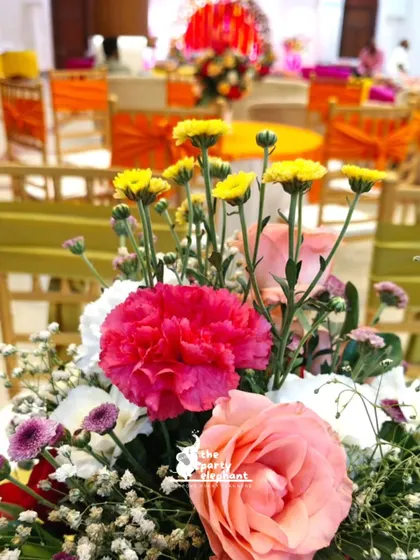 A close-up of a floral centerpiece from the Mehendi ceremony, featuring a bright mix of pink carnations, yellow chrysanthemums, and peach roses.