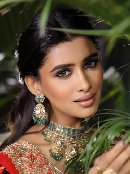 The greenery in the background beautifully contrasts with the red saree, making the bride's glowing skin and intense eyes the central focus.