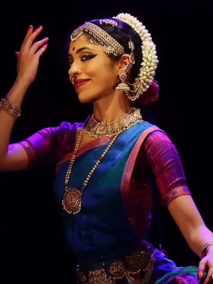A profile shot showing a soft, happy expression. The lighting highlights the traditional makeup and jewelry, which are essential to the character portrayal.