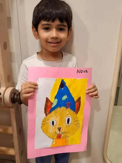 Another proud student showing off his completed cat artwork. Seeing their finished drawing, neatly mounted on colored paper, gives children a tangible sense of achievement.