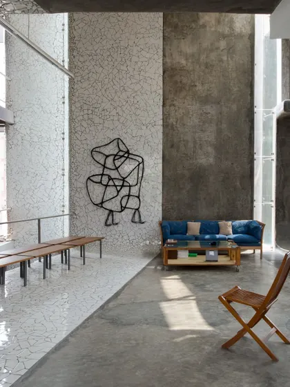 The Artrovert studio features a large, open-plan living and working area with high ceilings. The design uses raw concrete and white mosaic floors to create a durable and versatile space for an artist.