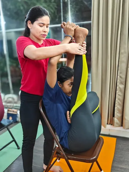Our instructors are trained to provide gentle and effective adjustments. Here, a student receives help in a seated forward bend variation using a chair.