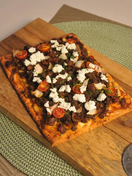 This is my minced meat flatbread, topped with feta cheese and cherry tomatoes. It's a rustic and hearty appetizer that is perfect for sharing.
