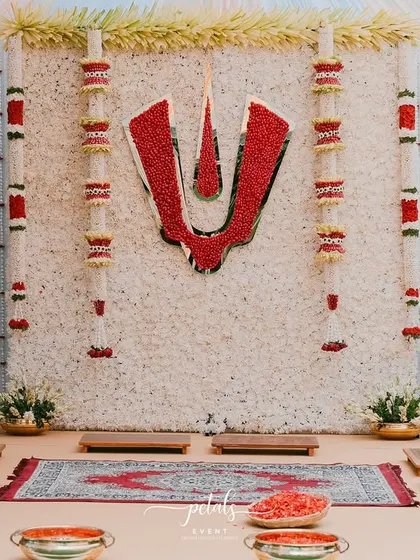 A closer look at the Nalugu ceremony backdrop, showcasing the intricate floral work. The Balaji Nama is meticulously crafted from red flowers against a dense wall of white chrysanthemums, flanked by traditional brass lotus props.