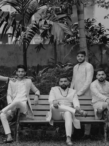 A cool, classic black and white portrait of the groom and his groomsmen, posing together in a garden.