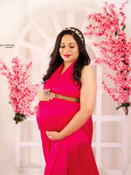 A gentle, loving portrait of an expectant mother in a flowing pink gown, surrounded by delicate pink floral decorations.