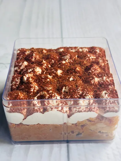 A side view of the Tiramisu Tres Leches tub, showing the coffee-soaked sponge fingers layered with creamy mascarpone.