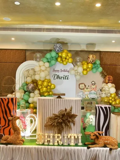 This jungle-themed decor uses animal print pedestals and cute cartoon animal props. The balloon arch in green and gold complements the wild and fun atmosphere.