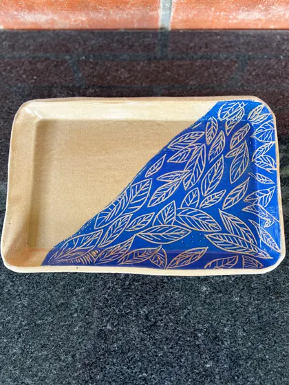 This rectangular tray features a beautiful sgraffito leaf pattern. A student carved this design through a layer of blue underglaze to reveal the clay color below.