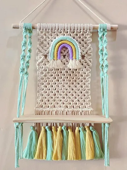 A cheerful wall shelf designed for a child's room. It features a pastel rainbow and colorful tassels, making it a fun place to store small toys or books.