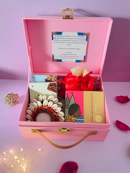 A single pink suitcase hamper, featuring a shell-work diya, a box of incense, and a satin potli. This is a great example of a thoughtful, budget-friendly gift.
