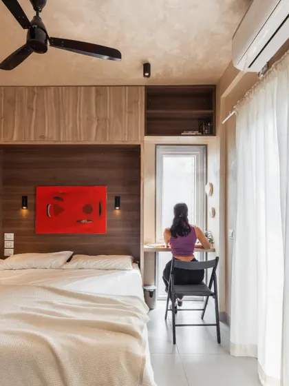 This bedroom in a compact apartment is designed for flexibility. It features a dedicated study nook by the window for work, ample wardrobe storage, and a Murphy bed that can be folded away to create open space for activities like yoga or workouts.